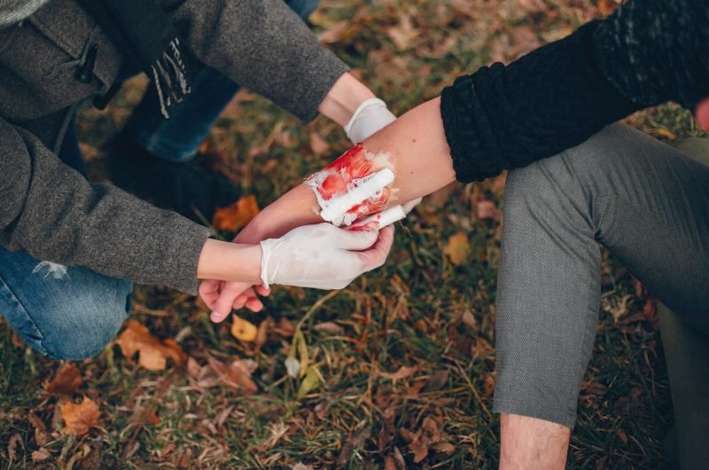 Guy bandages his friend’s hand Providing first aid in the park. Man bandaged  injured arm. Guy helps a friend.