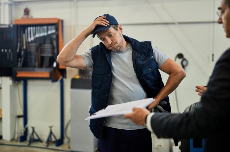 Distraught car mechanic going through problematic paperwork with his manager in auto repair shop.